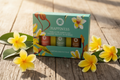 Coffret Happiness huiles essentielles posé sur fond bois avec fleurs tropicales
